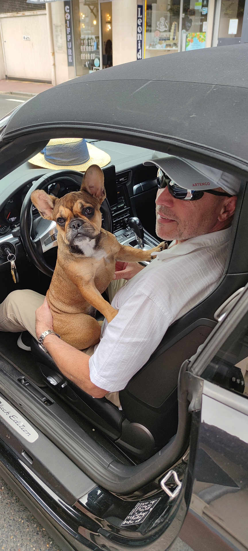 Seve Tataryn participe au concours pour gagner de l'argent avec cette photo : man, dog, french_bulldog, car, convertible, sunglasses, hat, street, window, dashboard, steering_wheel, keys, seat, clothing, pet, animal, outdoor, smile, casual, sunny