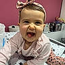 baby, bed, cheerful, child, clothing, cute, funny_face, girl, headband, indoor, infant, leaning, long_sleeve, person, pink, pink_wall, room, smile, star_pattern, tongue