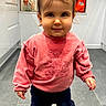 cabinet, casual, child, clothing, face, floor_tiles, girl, hair_ponytail, indoors, kitchen, light, navy_pants, person, pink_sweatshirt, smile, sneakers, standing, toddler, window, young_child