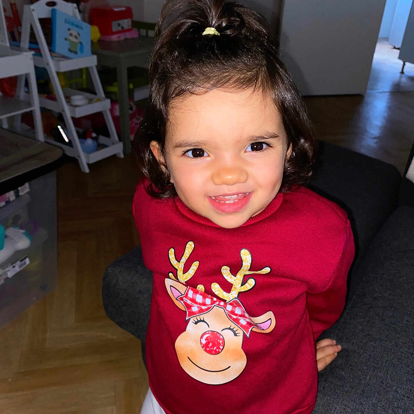 Waleina participe au concours pour gagner de l'argent avec cette photo : bright, child, cozy, cute, face, furniture, hair_tied, happy, holiday_theme, indoor, living_room, person, portrait, red_sweater, reindeer_design, smiling, toys, white_pants, wooden_floor, young_child