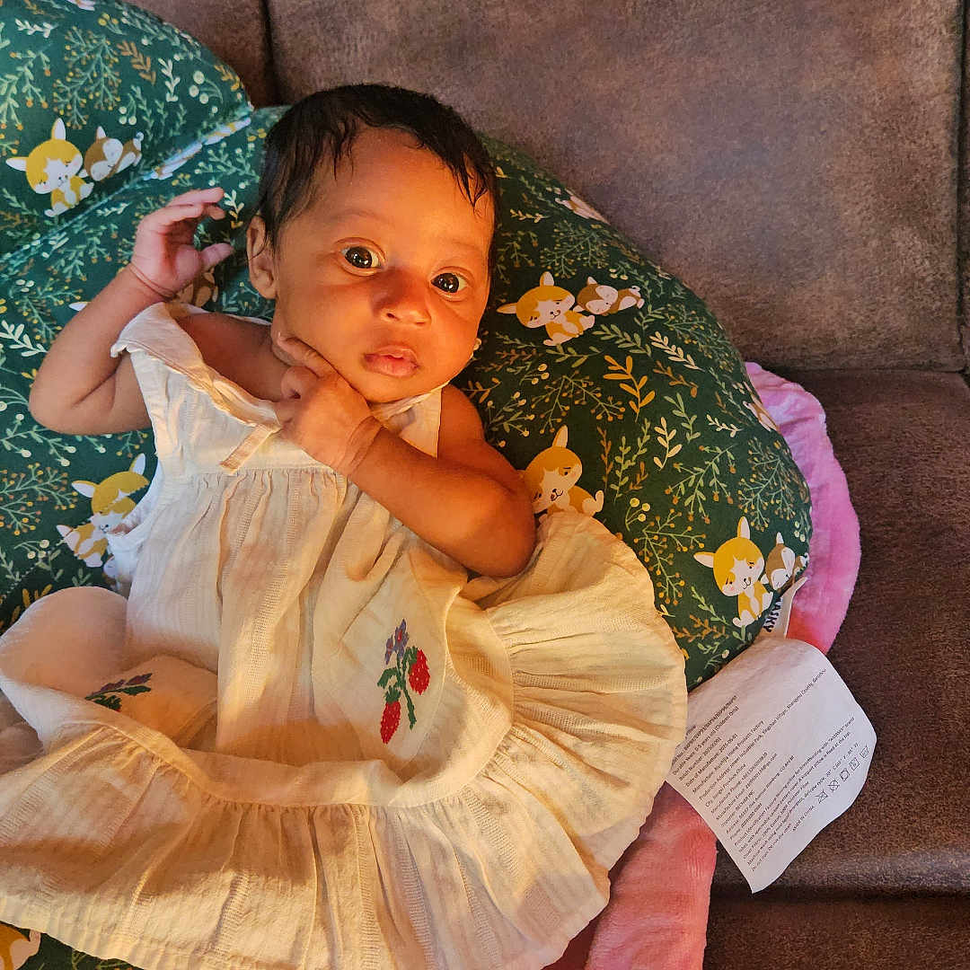 Jorjiana joined the competition — help win amazing prizes! baby, infant, dress, pillow, couch, blanket, foot, face, person, indoors, child, cute, green, pink, brown, pattern, comfort, relaxing, small, young