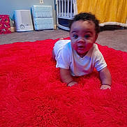 Ni'Amani is registered to the contest to win money with this photo: baby, baby_supplies, carpet, carpeted_floor, child, crawling, crib, curly_hair, floor, home, indoor, infant, nursery, person, plush, red_rug, room, wall_outlet, white_onesie, yellow_blanket