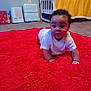 baby, baby_supplies, carpet, carpeted_floor, child, crawling, crib, curly_hair, floor, home, indoor, infant, nursery, person, plush, red_rug, room, wall_outlet, white_onesie, yellow_blanket