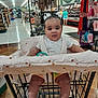 aisle, baby, child, clothing, cushion, cute, floor, grocery_store, hair_bow, indoor, infant, person, retail, shelf, shoes, shopping, shopping_cart, smiling, store, toy