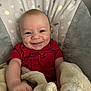baby, smiling, blanket, red_shirt, infant, cushion, baby_seat, happy, cute, child, face, skin, arm, indoor, soft_texture, comfort, portrait, young_child, clothing, seated