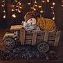 baby, blanket, brown_hat, wooden_toy, toy_truck, pinecones, fairy_lights, star_lights, wooden_floor, knitwear, infant, face, portrait, indoor, warm_lighting, decor, cozy, child, resting, cute
