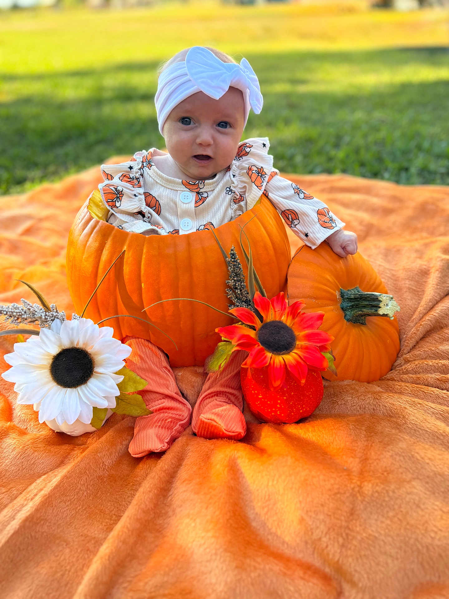 Wrenlee is registered to the contest to win money with this photo: baby, pumpkin, orange_blanket, flower, headband, outdoor, grass, fall, cute, infant, decor, costume, autumn, sitting, child, nature, portrait, seasonal, smiling, holiday