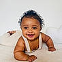 baby, smiling, curly_hair, gold_necklace, gold_bracelet, knitwear, lying_down, happy, cute, infant, soft_texture, portrait, child, toddler, skin, face, hand, background, indoor, expressive