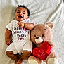 Dylan is registered to the contest to win money with this photo: baby, infant, smiling, onesie, teddy_bear, stuffed_animal, heart, love, happy, cute, soft_blanket, lying_down, child, joyful, celebration, father's_day, cuddly, toy, portrait, indoors