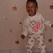 Lilou a rejoint le concours — aidez-le/la à gagner de superbes lots ! casual, cat_print, child, clothing, cute, happy, indoor, pants, patterned_wall, person, playful, portrait, smiling, standing, sweatshirt, tile_floor, toddler, wallpaper, white_shoes, young_child