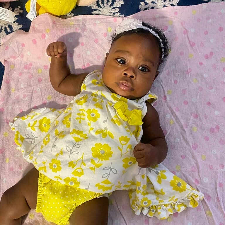 Kalani is registered to the contest to win money with this photo: baby, blanket, child, colorful, cute, girl, headband, indoors, infant, lying_down, pineapple_toy, pink_flamingo_toy, playful, plush_toys, polka_dot, portrait, smiling, soft_toys, yellow_dress, young
