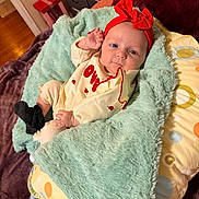 Evelynne joined the competition — help win amazing prizes! baby, infant, child, headband, red_bow, blanket, plush_blanket, pillow, onesie, sock, hand, face, eyes, lying_down, bed, dresser, hardwood_floor, gift_box, cozy, indoor