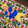 baby, blue_top, butterflies, child, closeup, colorful, cute, floral_blanket, happy, indoors, infant, lying_down, person, playful, portrait, smile, socks, toddler, yellow_headband, yellow_pants
