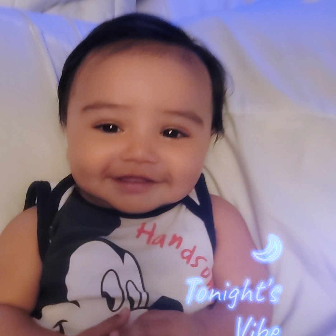 Ian joined the competition — help win amazing prizes! baby, smiling, infant, bed, bedding, blanket, cartoon_clothing, cute, happy, face, child, indoors, portrait, hands, lying_down, dark_hair, soft_lighting, text_overlay, moon, cozy