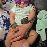 Ian is registered to the contest to win money with this photo: adult, baby, casual, child, cute, fashion_accessory, hand, home, indoor, mittens, nails, orange_nails, person, portrait, relaxed, seated, striped_clothing, sunglasses, towel, wicker_chair