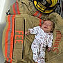 baby, clothing, cute, fabric, firefighter_helmet, firefighter_jacket, helmet_badge, indoor, infant, orange_stripes, person, protective_gear, rescue, resting, safety, sleeping, small, textile, uniform, white_onesie