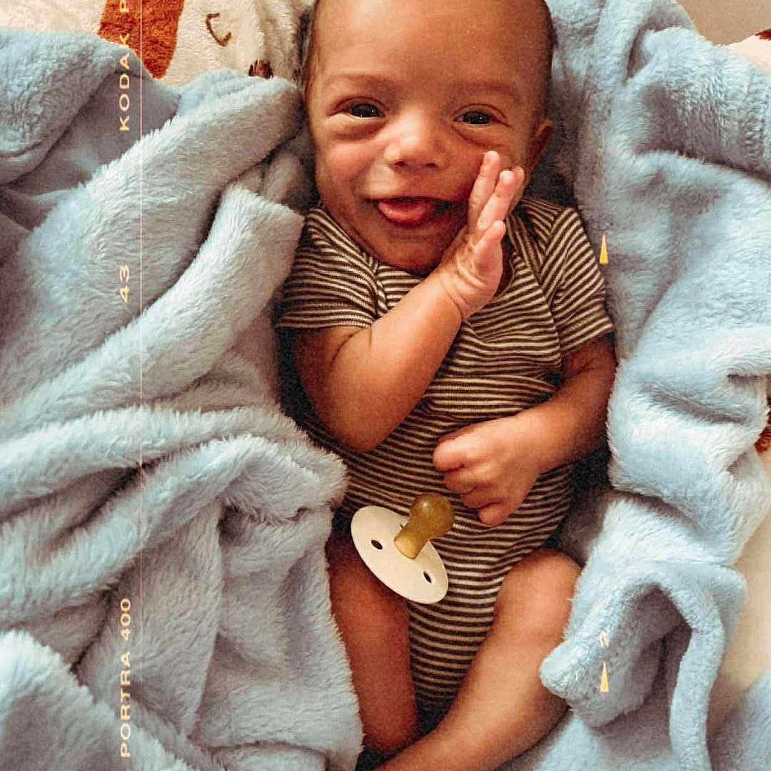 John Luke joined the competition — help win amazing prizes! baby, blanket, child, cozy, cute, face, foot, hand, happy, infant, lying_down, newborn, pacifier, portrait, skin, smile, soft_texture, striped_clothing, warm_colors, wrapped