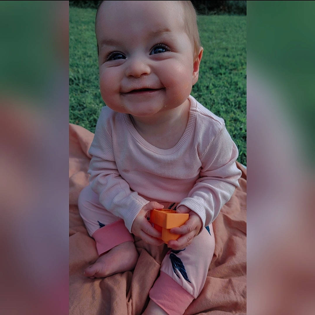 Kiara is registered to the contest to win money with this photo: baby, baby_laughing, baby_toddler_clothing, child, face, facial_expression, finger, gesture, grass, happy, iris, joy, lip, nose, people_in_nature, person, plant, skin, sleeve, smile