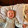baby, smiling, infant, pajamas, bed, pillow, happy, face, child, sleepwear, person, wooden_headboard, cozy, indoor, cute, young_child, portrait, lying_down, blanket, home