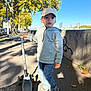 blue_sky, cap, child, curious, daylight, graffiti, hoodie, jeans, outdoor, person, play, scooter, shadow, sidewalk, sneakers, street, trees, urban, wall, young