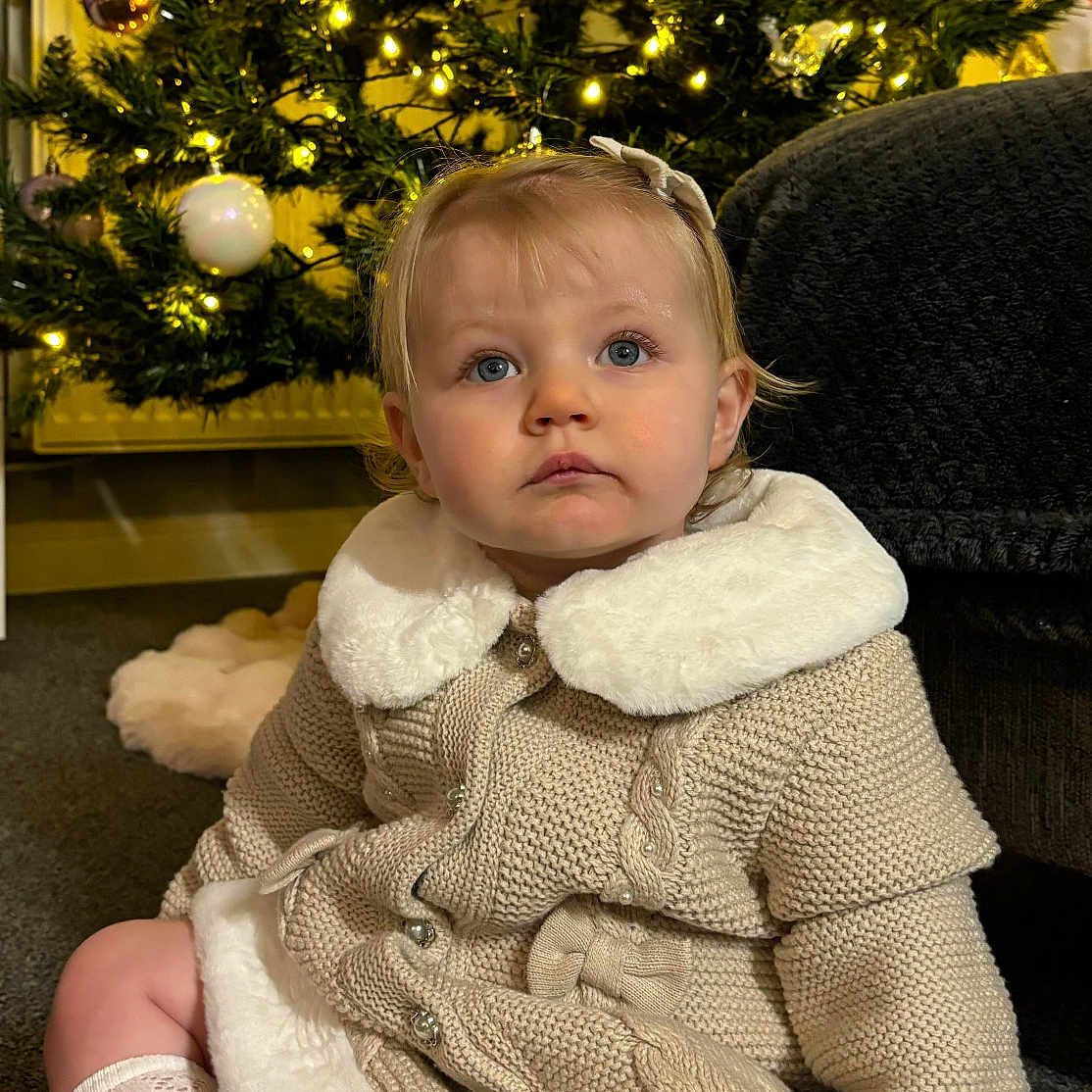 Leila is registered to the contest to win money with this photo: baby, bodypart, clothing, couch, face, finger, fir, furniture, hand, hat, head, hosiery, knitwear, person, photography, plant, portrait, sock, sweater, tree