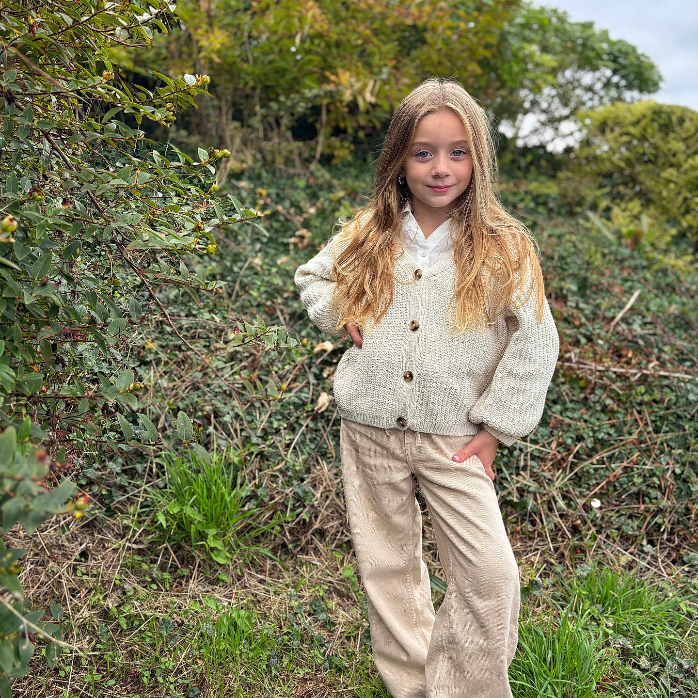 Zahya a rejoint le concours — aidez-le/la à gagner de superbes lots ! blonde, cardigan, casual_clothing, child, cloudy_sky, fashion, girl, grass, greenery, long_hair, nature, outdoor, pants, plants, portrait, shoes, smile, standing, trees, young