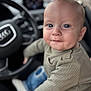 baby, child, infant, car_interior, steering_wheel, seat, clothing, long_sleeve, jeans, socks, portrait, close_up, face, expression, curious, indoor, blurred_background, automobile, person, cute