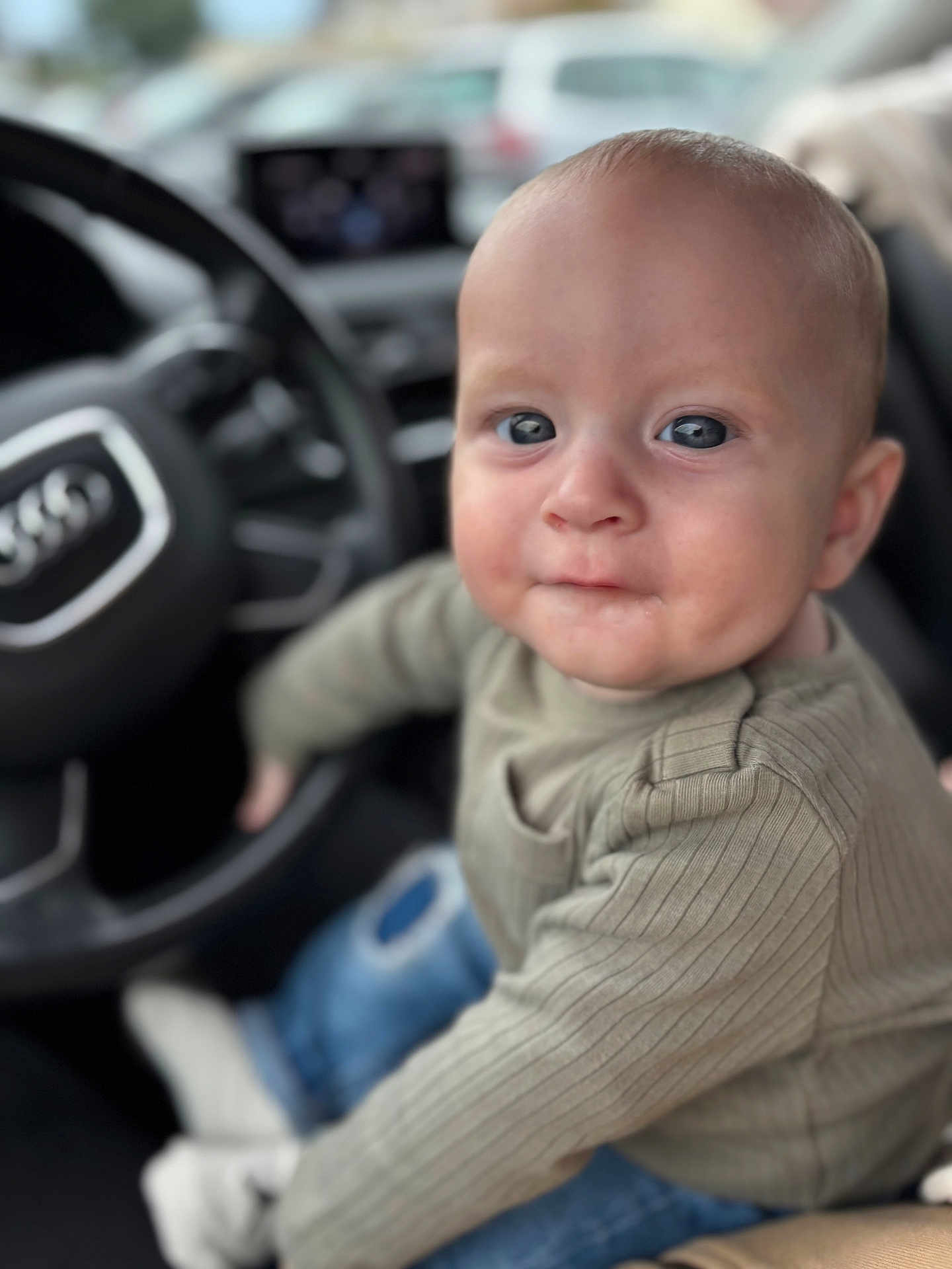 Kaïs participe au concours pour gagner de l'argent avec cette photo : baby, child, infant, car_interior, steering_wheel, seat, clothing, long_sleeve, jeans, socks, portrait, close_up, face, expression, curious, indoor, blurred_background, automobile, person, cute