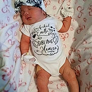 Serenity is registered to the contest to win money with this photo: baby, newborn, infant, sleeping, headband, bow, onesie, blanket, mittens, heart_pattern, soft_fabric, portrait, cozy, legs, arms, skin, peaceful, clothing_text, closeup, nursery