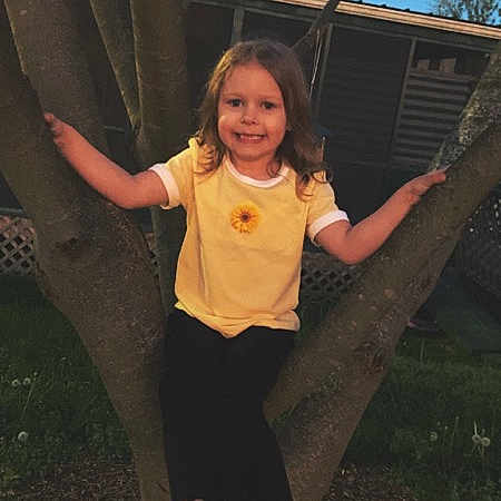 Amaya is registered to the contest to win money with this photo: child, tree, yellow_shirt, black_pants, smile, outdoor, nature, sunflower, house, grass, branches, sandals, footwear, daylight, portrait, person, happy, casual_clothing, play, young