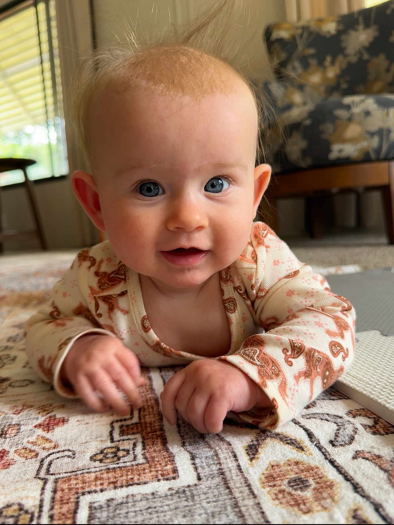 Nora joined the competition — help win amazing prizes! baby, infant, blue_eyes, hands, lying_down, patterned_rug, indoor, furniture, window, curious, child, cute, person, soft_lighting, long_sleeve, clothing, face, head, skin, expression