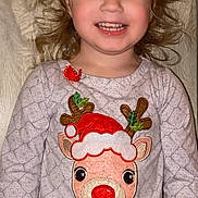 Kinsley is registered to the contest to win money with this photo: child, smiling, curly_hair, reindeer, festive_clothing, red_nose, santa_hat, long_sleeve_shirt, patterned_shirt, wooden_background, happy, portrait, indoor, cute, holiday_theme, girl, person, face, clothing, red_polka_dot