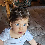 Mia participe au concours pour gagner de l'argent avec cette photo : toddler, child, blue_eyes, curly_hair, white_shirt, pink_leggings, sitting, floor_tiles, indoor, armchair, floral_pattern, wooden_chair, home, portrait, cute, young_child, person, natural_light, happy, casual_clothing