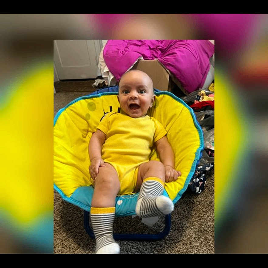 Geziel joined the competition — help win amazing prizes! baby, infant, child, smiling, sitting, yellow_outfit, striped_socks, bouncer, chair, indoor, portrait, happy, open_mouth, feet, legs, colorful, blurred_background, carpet, furniture, playful