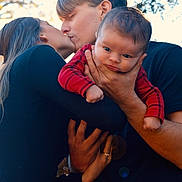 Baylor is registered to the contest to win money with this photo: baby, child, couple, kiss, love, family, outdoor, nature, sunlight, trees, affection, holding, portrait, red_clothing, black_clothing, hands, face, young_adult, toddler, intimate