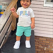 Jasani is registered to the contest to win money with this photo: toddler, child, smile, cap, tshirt, shorts, sneakers, porch, railing, house, brick, window, outdoor, happy, person, clothing, footwear, daylight, standing, casual