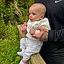 baby, person, child, tattoo, hand, clothing, white_sock, white_pants, white_jacket, outdoor, wooden_railing, greenery, flowers, forest, nature, portrait, holding, cute, curious, infant