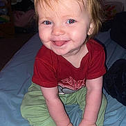 Delilah joined the competition — help win amazing prizes! baby, child, smiling, tongue_out, sitting, clothing, red_shirt, green_pants, pink_socks, bed, blanket, indoor, human, cute, happy, portrait, toddler, hands, face, hair