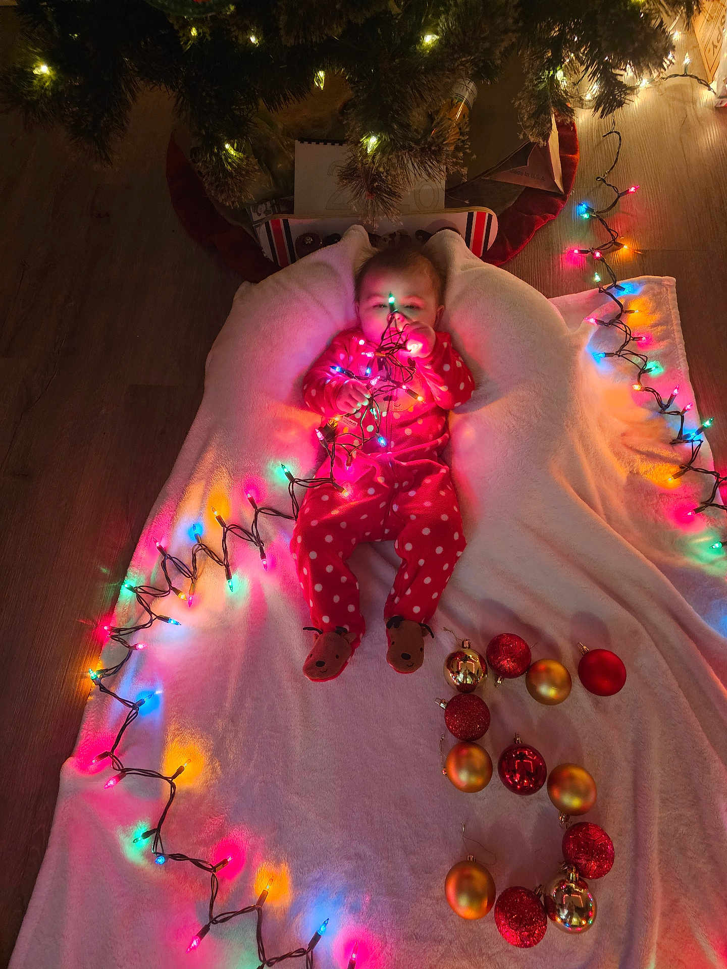 Chloe joined the competition — help win amazing prizes! baby, christmas_tree, christmas_lights, blanket, floor, ornaments, red_pajamas, polka_dots, holiday, festive, indoor, child, toy, decorations, soft_lighting, wooden_floor, feet, face, cute, toddler