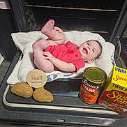 Chloe is registered to the contest to win money with this photo: baby, blanket, can, container, cooking, floor, food, four_months, happy, infant, kitchen, lying_down, oven, potatoes, red_onesie, smiling, stove_top, stuffing, wood_floor, yams