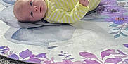 Chloe is registered to the contest to win money with this photo: baby, carpet, child, close_up, cozy, curious_expression, cute, floor, home, indoor, infant, lying_down, person, portrait, purple_flowers, round_mat, small_hands, soft_lighting, striped_clothing, yellow_onesie