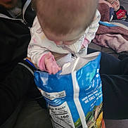 Chloe is registered to the contest to win money with this photo: baby, child, chips, couch, blanket, pajamas, snack, food_package, person, indoor, relaxed, curious, seated, young_child, family, living_room, home, casual, unfocused, cozy