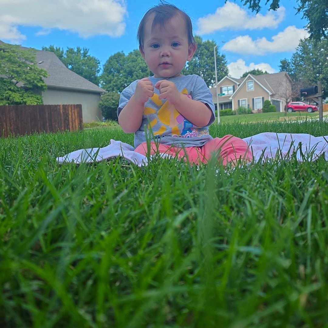 Scarlett is registered to the contest to win money with this photo: baby, blanket, blue_sky, casual_clothing, child, clouds, daytime, grass, greenery, house, lawn, nature, outdoor, person, portrait, suburban, summer, toddler, tree, young_child