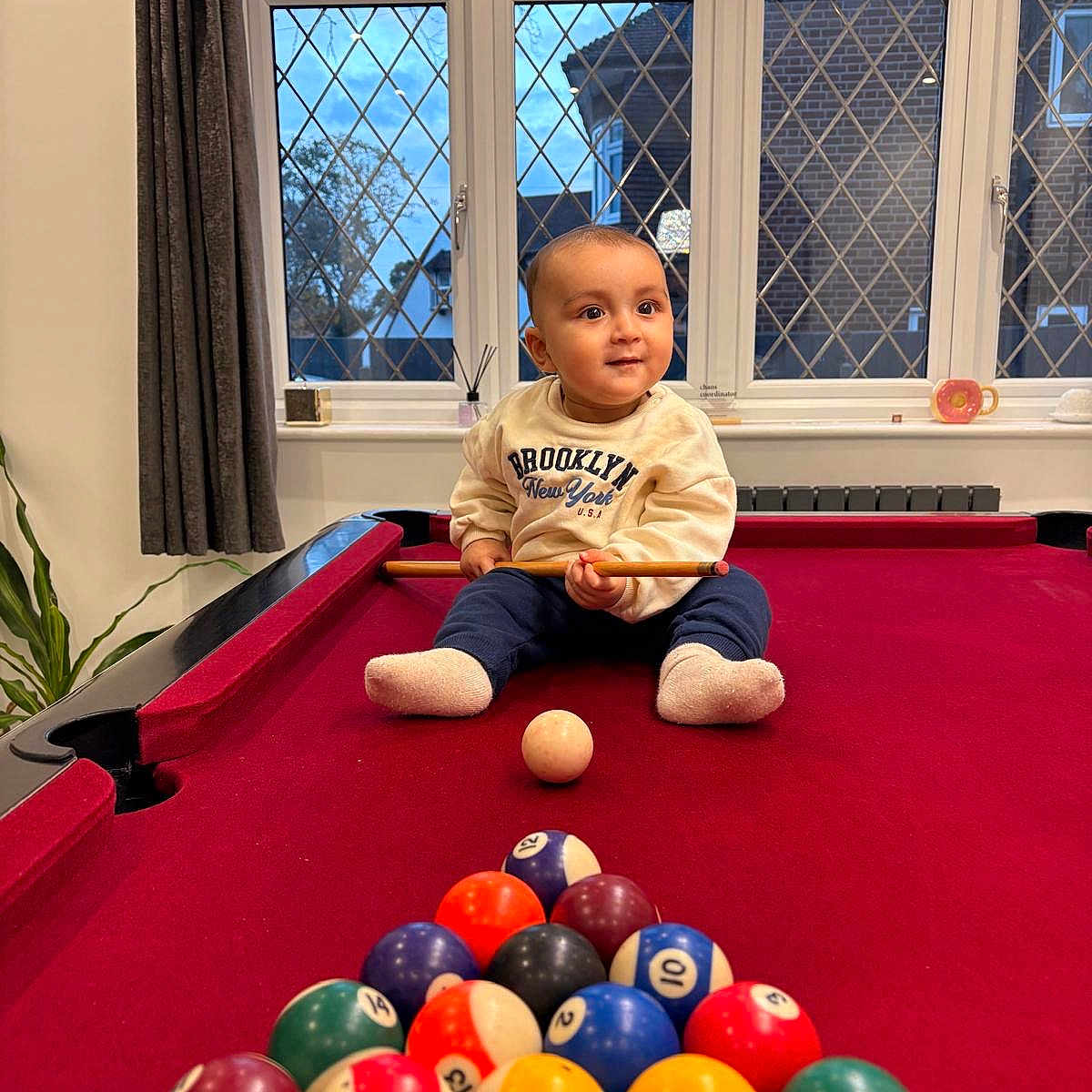 Asees joined the competition — help win amazing prizes! baby, billiard_balls, child, cue_stick, curtains, daylight, floor, furniture, home, indoor, pants, person, playful, pool_table, recreation, seated, socks, sweatshirt, toy, window
