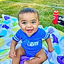 baby, smiling, blue_clothing, onesie, sitting, blanket, colorful, outdoor, grass, happy, child, face, foot, hand, water_bottle, shoes, sportswear, detroit_lions, infant, sunlight