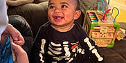 Eli joined the competition — help win amazing prizes! baby, child, smiling, skeleton_outfit, socks, person, indoor, toy, furniture, adult, phone, happy, playing, living_room, couch, colorful, curly_hair, casual_clothing, interaction, family