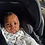 baby, car_seat, blanket, pacifier, infant, child, clothing, black_clothing, seatbelt, car_interior, sunlight, portrait, face, expression, indoor, hand, fabric, comfort, seat, travel