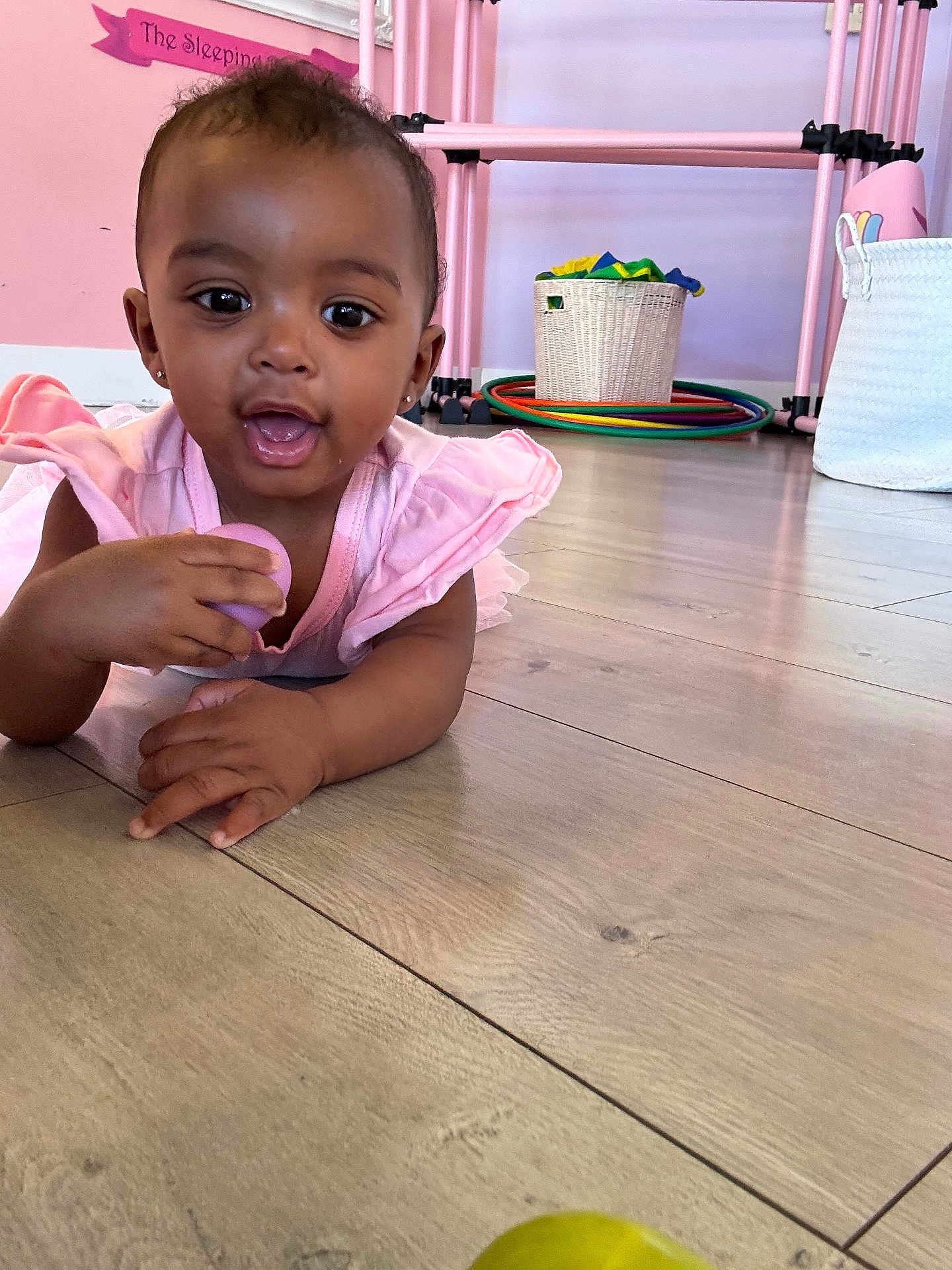 Taelor Burch joined the competition — help win amazing prizes! baby, child, pink_dress, toy, floor, wooden_floor, indoor, basket, hula_hoops, playful, happy, smiling, girl, earrings, pastel_colors, furniture, flooring, crawling, person, toddler