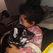 Vergil joined the competition — help win amazing prizes! child, puppy, dog, hug, curly_hair, indoor, colorful_collar, pink_shirt, patterned_clothing, black_dog, white_paws, cute, affection, portrait, cozy, furniture, table, relaxing, home, love