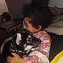 child, puppy, dog, hug, curly_hair, indoor, colorful_collar, pink_shirt, patterned_clothing, black_dog, white_paws, cute, affection, portrait, cozy, furniture, table, relaxing, home, love